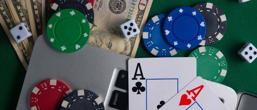 cards, chips, money and dice on top of computer and green felt
