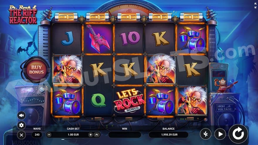 Five slot reels on a stage with speakers and amplifiers.